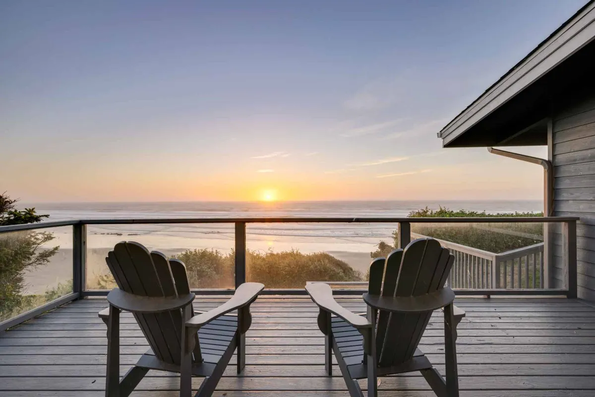 An inviting wooden deck with Adirondack chairs faces a breathtaking ocean sunset. The outdoor seating is designed for relaxation, whether sipping morning coffee or toasting the day's end, with nothing but the sea in front.