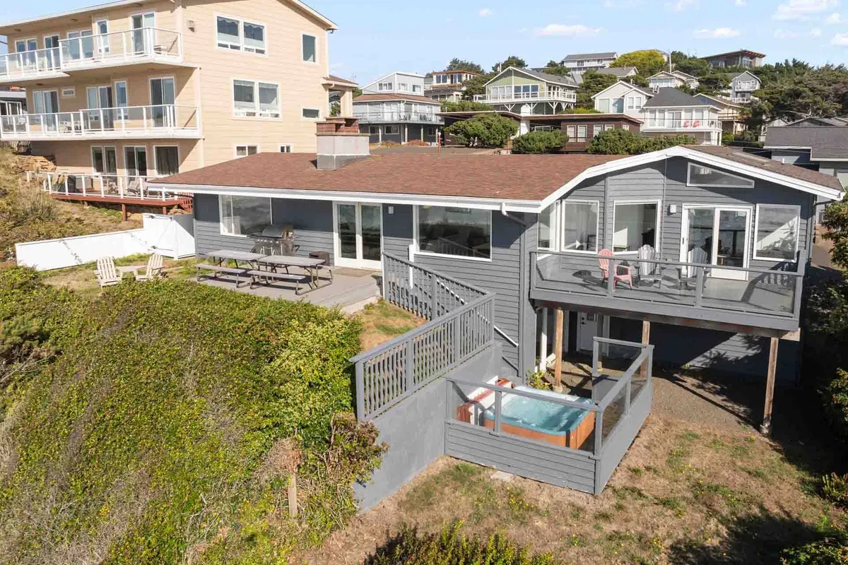 A spacious deck with a hot tub facing the ocean, surrounded by large windows and an outdoor seating area. The scene blends relaxation with breathtaking ocean vistas, inviting guests to unwind after a day at the beach in the wind-screened hot tub—a highlighted guest favorite.