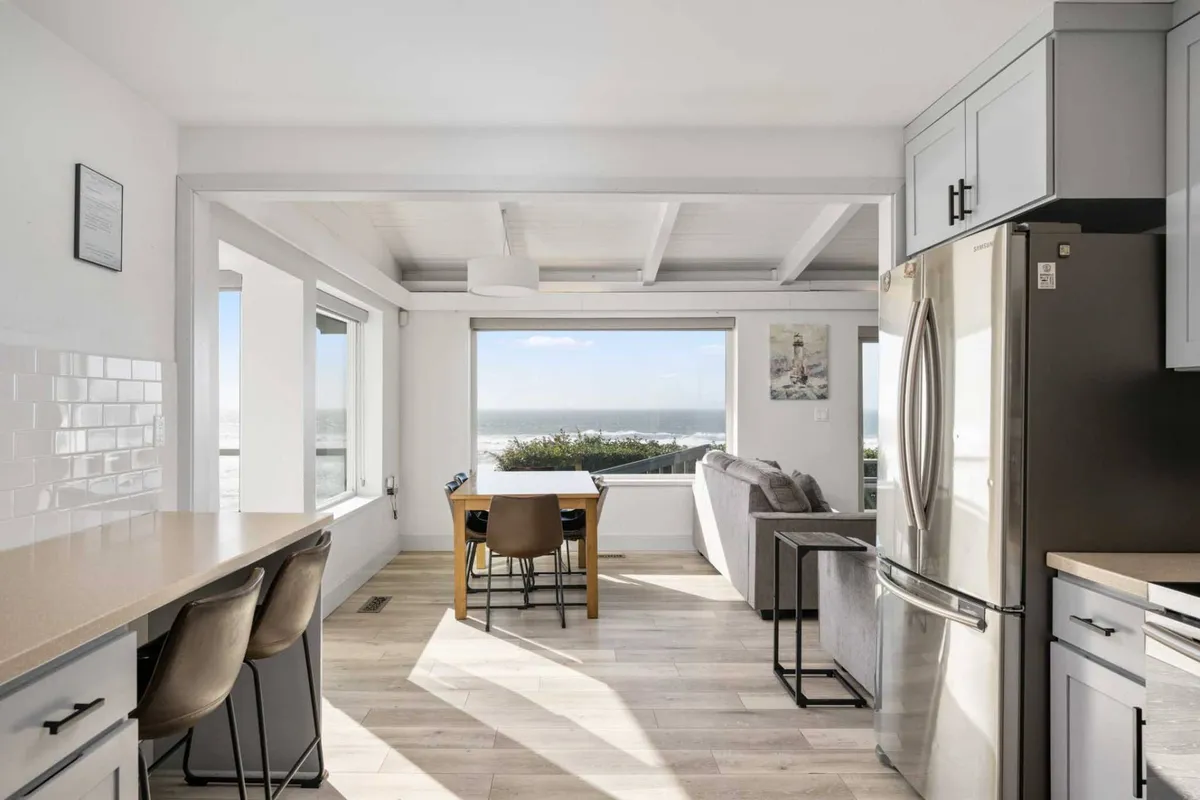This image features a large window offering a spectacular ocean view, with a dining table and a sofa positioned to enjoy both the scenery and social gatherings. The light floods in, creating an uplifting and tranquil atmosphere perfect for family meals or relaxing together.