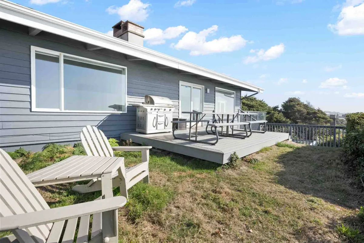 The image features a welcoming deck complete with Adirondack chairs, a grill, and sweeping landscape views. The inviting outdoor space is perfect for relaxing, outdoor dining, and letting pets safely enjoy the fresh air and scenic surroundings.