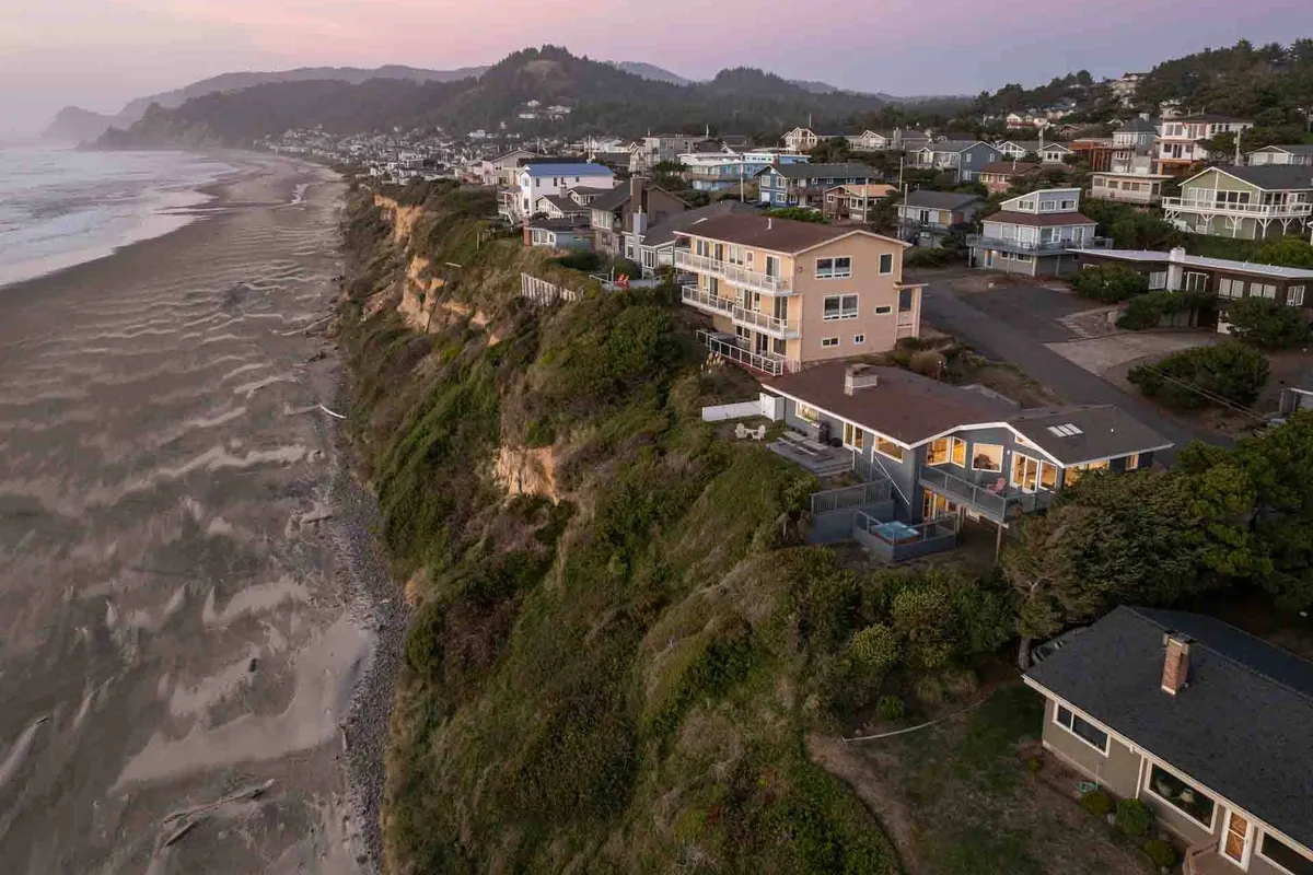 This exterior image showcases cliffside homes perched above the Pacific Ocean, with rugged coastline, rolling waves, and lush coastal vegetation in the foreground. The horizon stretches into the distance under a calm sky, setting a tranquil, nature-focused atmosphere.
