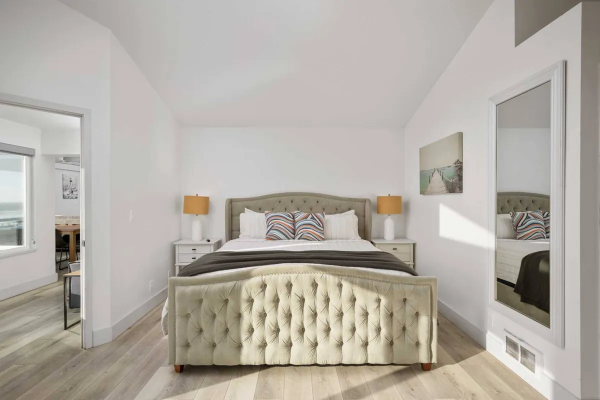 A cozy bedroom with a plush bed, two nightstands, and elegant mirrors above each. Soft lighting and neutral tones create a welcoming atmosphere, perfect for restful nights or quiet mornings.