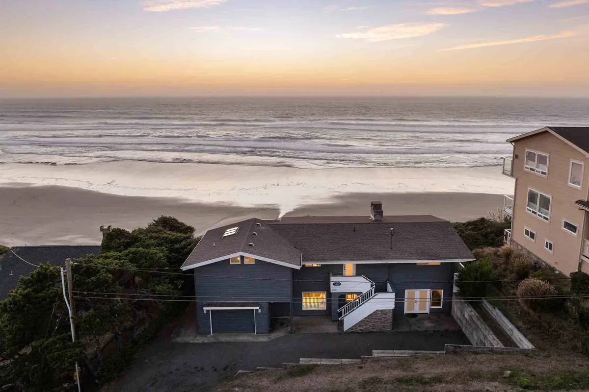 This exterior image highlights the house overlooking the vast Pacific Ocean with the sun setting over the water. The scene captures a tranquil and inviting beachside atmosphere, with the home nestled just steps away from the sand—perfectly embodying the promise of easy beach access and stunning sunset views.
