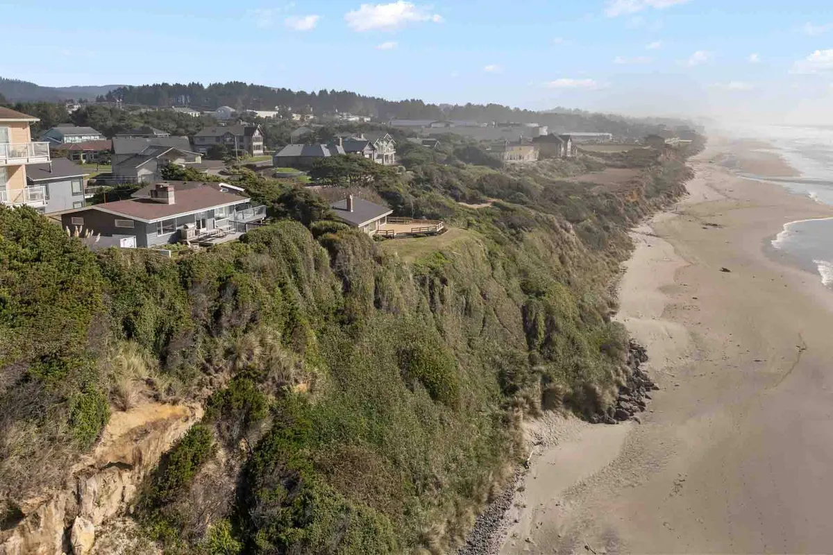 A sweeping view from the cliffs, showing cliffside houses, a sandy beach below, and the expansive ocean beyond. The area is bathed in soft light, highlighting prime locations for walks, photography, and nature exploration.