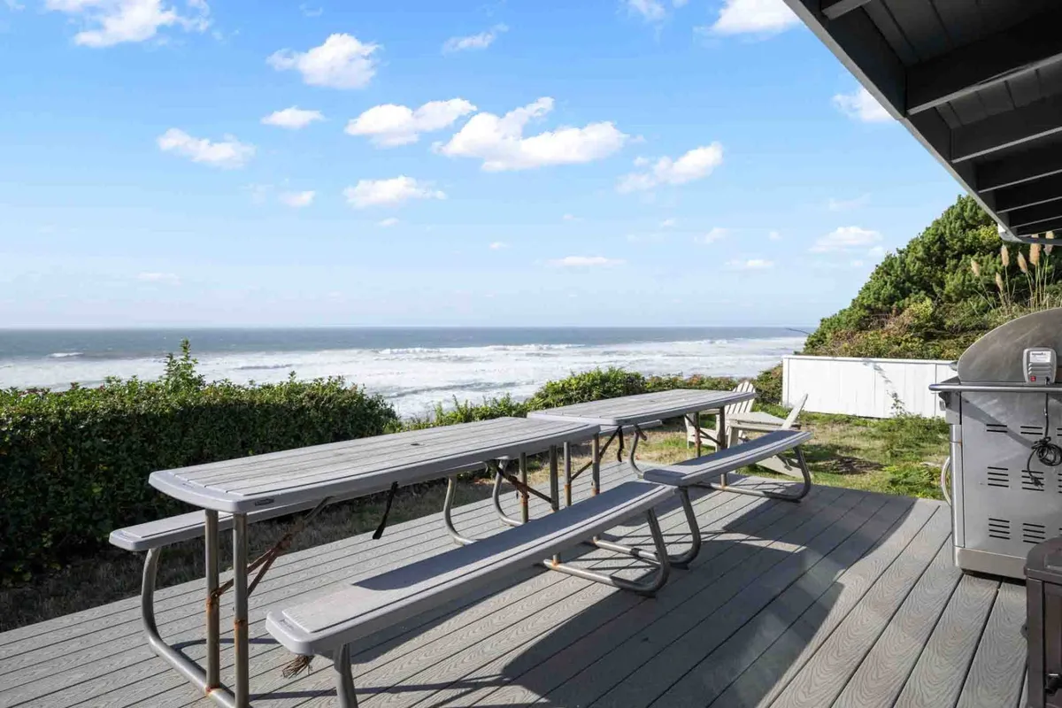 This image captures an inviting outdoor seating area on a deck with a grill, overlooking a stunning ocean view. The ambiance is tranquil yet joyful, with the setting sun casting a golden glow across the sky and deck. The scene suggests a space perfect for barbecuing, family gatherings, and relaxed socializing while immersed in natural coastal beauty.