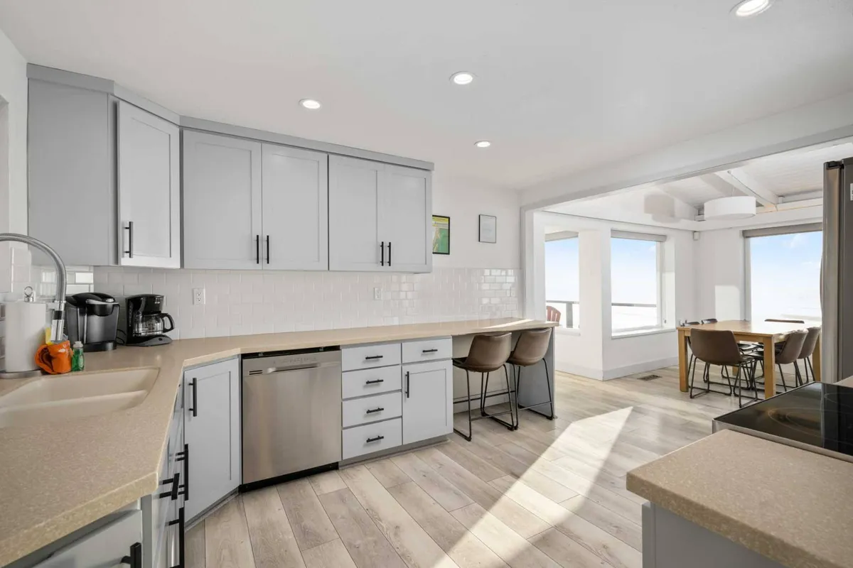 A modern kitchen with sleek cabinetry and stainless steel appliances extends into an open dining area, all oriented toward large windows that capture the stunning water views. The layout encourages group cooking, entertaining, and shared moments.